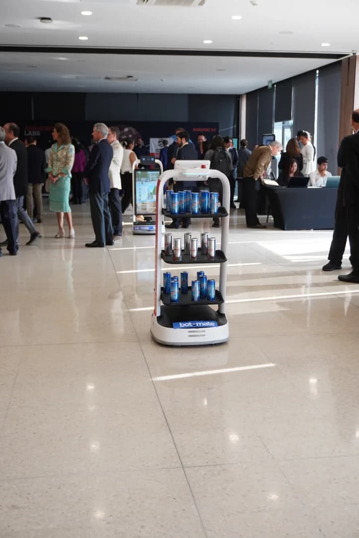 Robot con bandejas de bebidas frente a asistentes en un evento interior